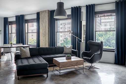 A black couch with a wooden coffee table in front of a window with a chair and a floor lamp.