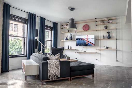 A living room with a black couch and a grey blanket.