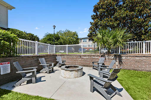 A fire pit surrounded by chairs in a sunny outdoor area.