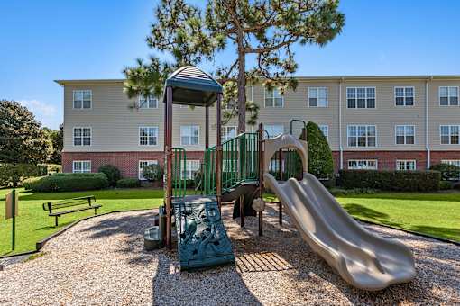 A playground with a slide and a swing set in front of a building.