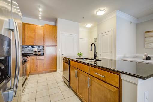 Apartments Near National Harbor - Tribeca at Camp Springs - A kitchen with wooden cabinets and a black countertop