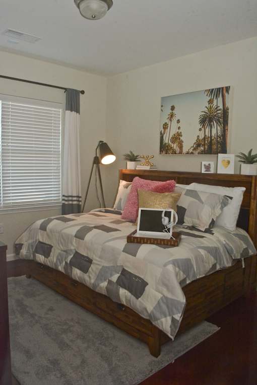 A bed with a grey and white comforter and a pink pillow on it.