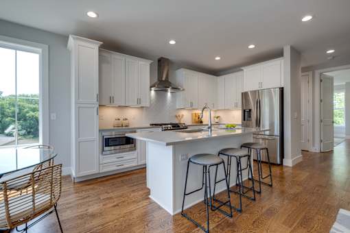 A modern kitchen with white cabinets and a wooden floor.
