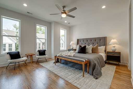 A bedroom with a bed, two chairs, and a ceiling fan.