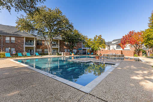 A large outdoor swimming pool surrounded by trees and apartment buildings.
