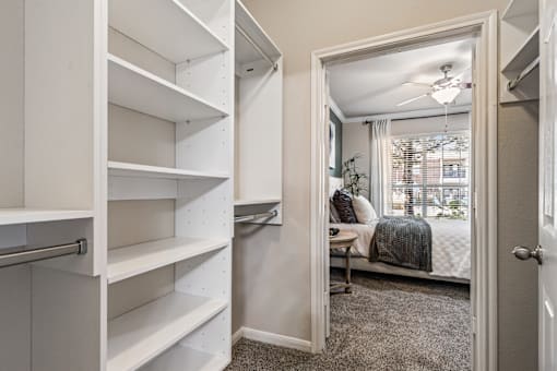 A white closet with shelves and a mirrored doorway leading to a bedroom.