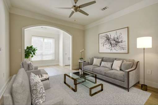 Apartments Near Washington D.C. - Tribeca at Camp Springs - A living room with a grey sofa, a coffee table, and a large painting on the wall