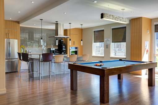 A pool table is in the middle of a room with a kitchen in the background.