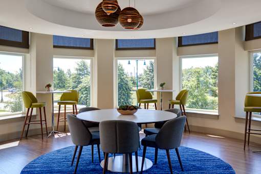 A round table with grey chairs is in the middle of a room with a blue rug.