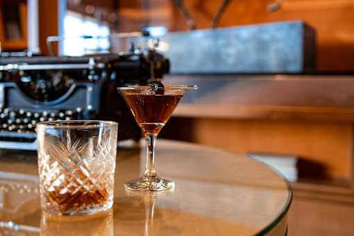 A cocktail glass with a drink in it sits on a table next to a glass with a drink in it.