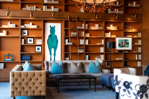 A living room with a brown tufted chair, a blue couch, and a painting of a green horse on the wall.
