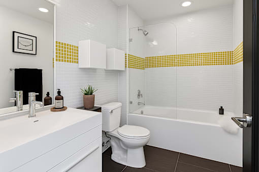 A white toilet sits in a bathroom with a yellow and white tile wall.