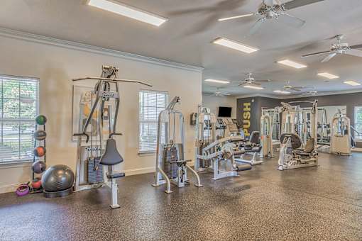 A gym with a variety of exercise equipment including a weight rack, a leg press machine, a treadmill, and a stationary bike.