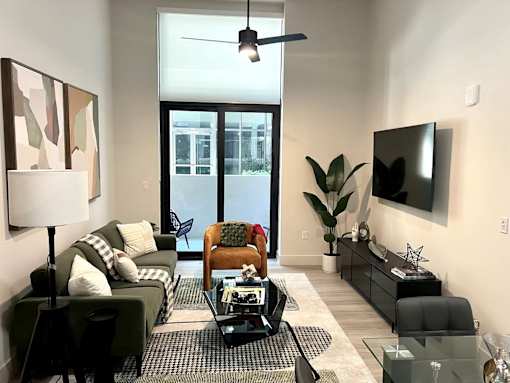 A living room with a black couch, a glass coffee table, and a flat screen TV mounted on the wall.