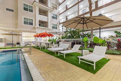 A pool area with a white chair and a brown umbrella.