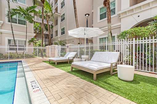 A pool with a white umbrella and two lounge chairs.