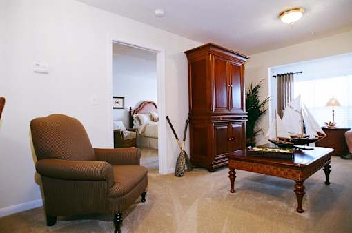 A brown chair is in a living room with a wooden cabinet and a table with a ship model on it.