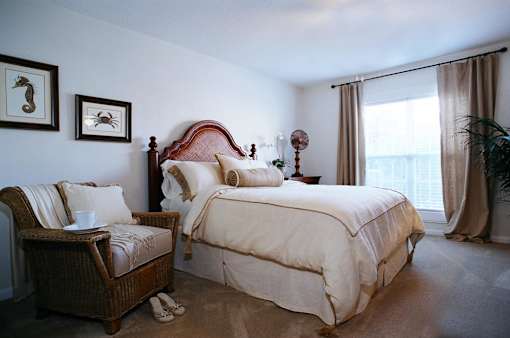 A bedroom with a bed, chair, and two pictures on the wall.