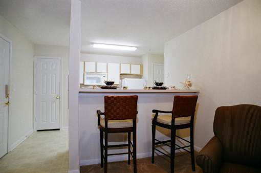 A kitchen with a white counter and brown chairs.