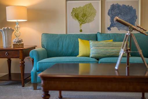 A blue couch with a yellow pillow and a lamp on a side table.