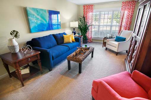 A living room with a blue couch, a red chair, and a painting on the wall.
