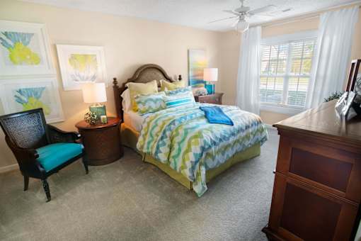 A bedroom with a bed, chair, and painting.