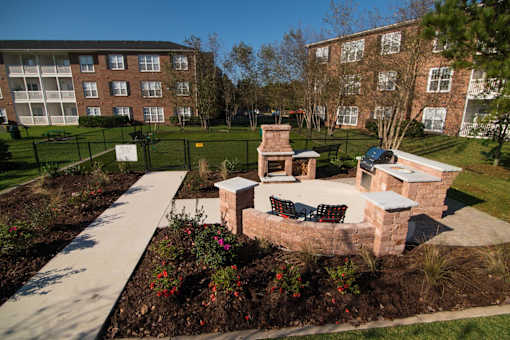 A brick patio with a fireplace and seating area in the foreground with apartment buildings in the background.