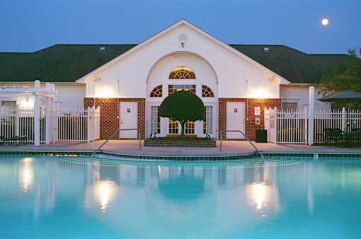 A pool in front of a building with lights on.