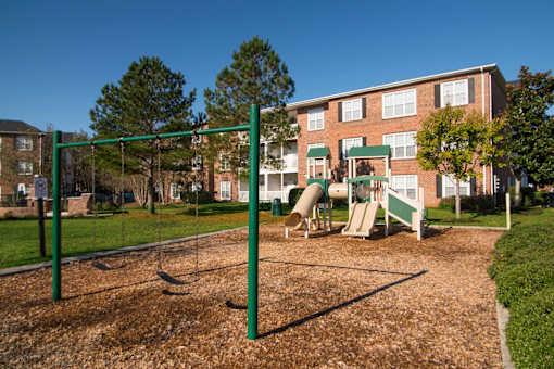 A playground with a swing set and a slide in front of a brick building.