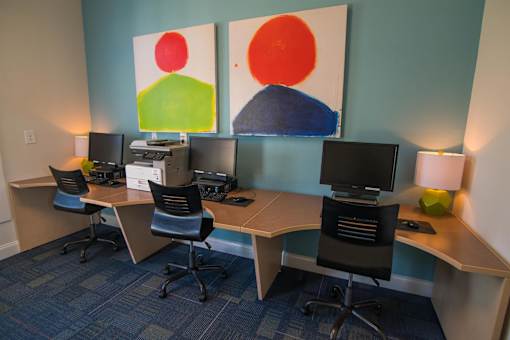 Two desks with computers and chairs in front of two paintings.