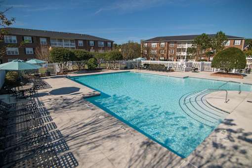 A large outdoor swimming pool surrounded by a fence and chairs.
