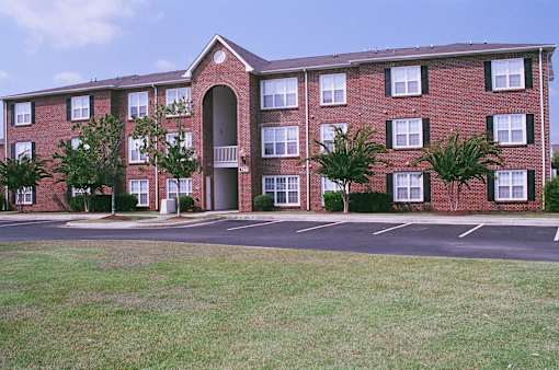 A red brick building with a large arched entrance and a parking lot in front.
