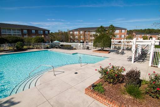 A swimming pool surrounded by a white fence and a brick flower bed.