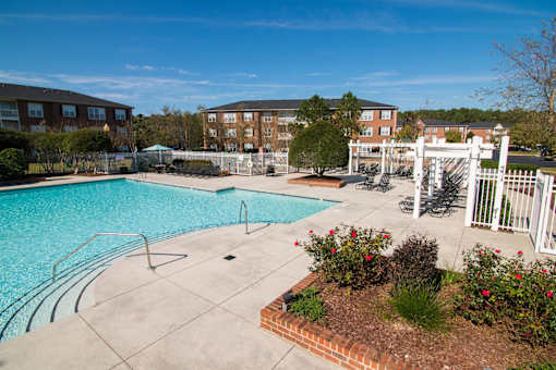 A pool surrounded by a white fence and a brick flower bed.
