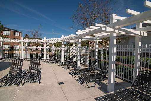 A white pergola with black metal chairs is set up in a courtyard.