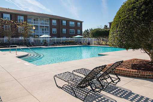 A pool area with chairs and a building in the background.