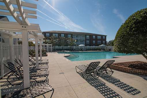 A pool area with sun loungers and a building in the background.