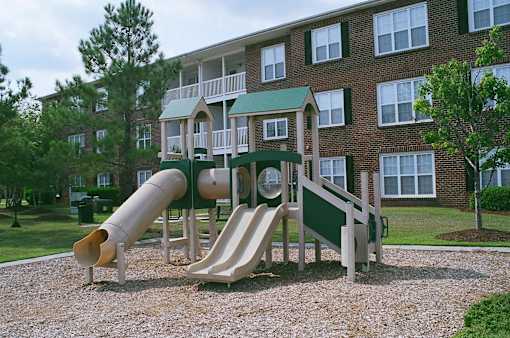 A playground with a green slide and a brown slide in front of a brick building.