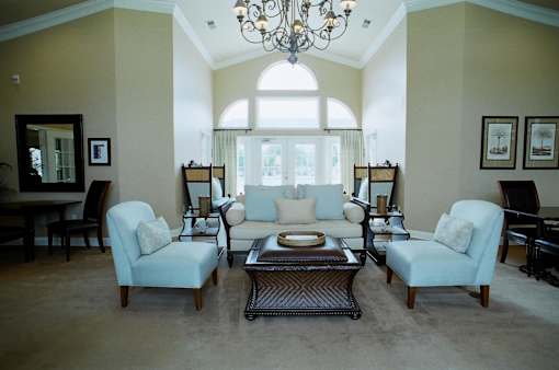 A living room with a chandelier, two chairs, a couch, a coffee table, and pictures on the wall.