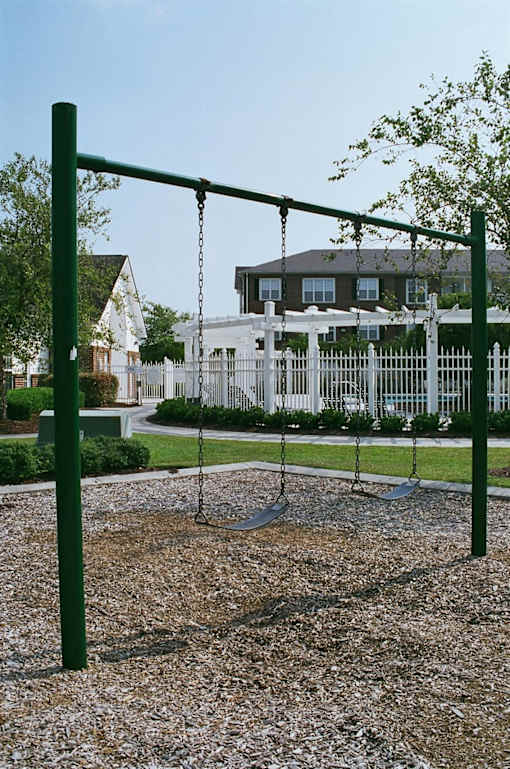 A playground with a swing set and a white fence in the background.