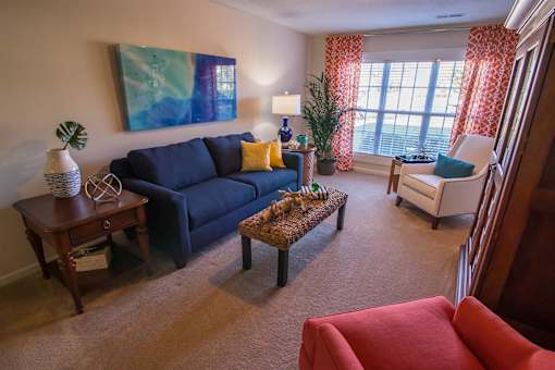 A living room with a blue couch, a red chair, and a painting on the wall.