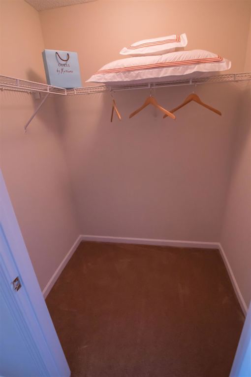 A small closet with a shelf and clothes hanging.
