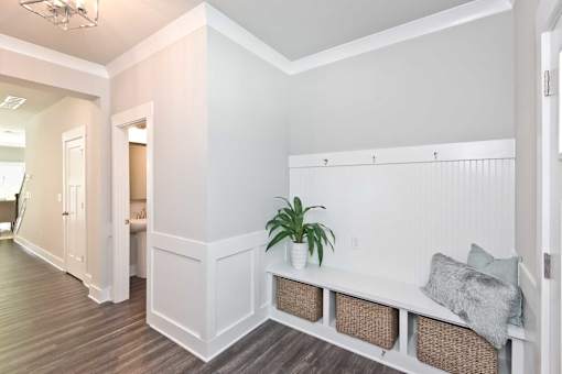 A white bench with baskets underneath is in a room with wood flooring.