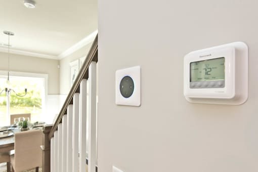A wall-mounted thermostat and a wall-mounted smoke detector are installed on a wall.