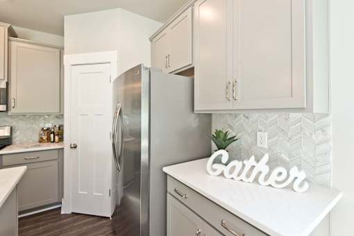 A kitchen with a refrigerator and a countertop with a sign that says "Gather".