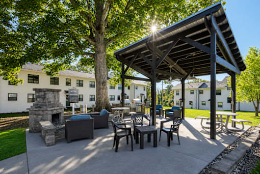 A sunny day at a park with a pavilion, chairs, and a fireplace.