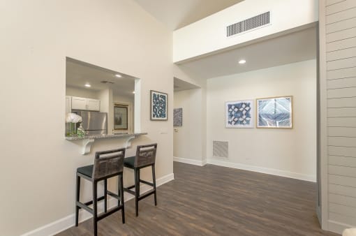 a living room with two stools in front of a kitchen with a bar area