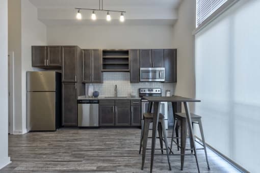 Three BR Apartments in Germantown Nashville TN - Peyton Stakes - Rustic-Style Kitchen with Wood Cabinetry, Silver Appliances, Seating Bar, Overhead Lights, Dark Theme, and Tile Backsplash
