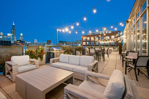 a rooftop terrace with couches and tables and a city at night