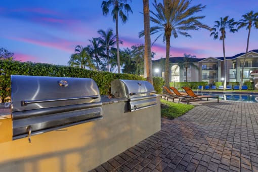 two bbq grills near a pool with palm trees